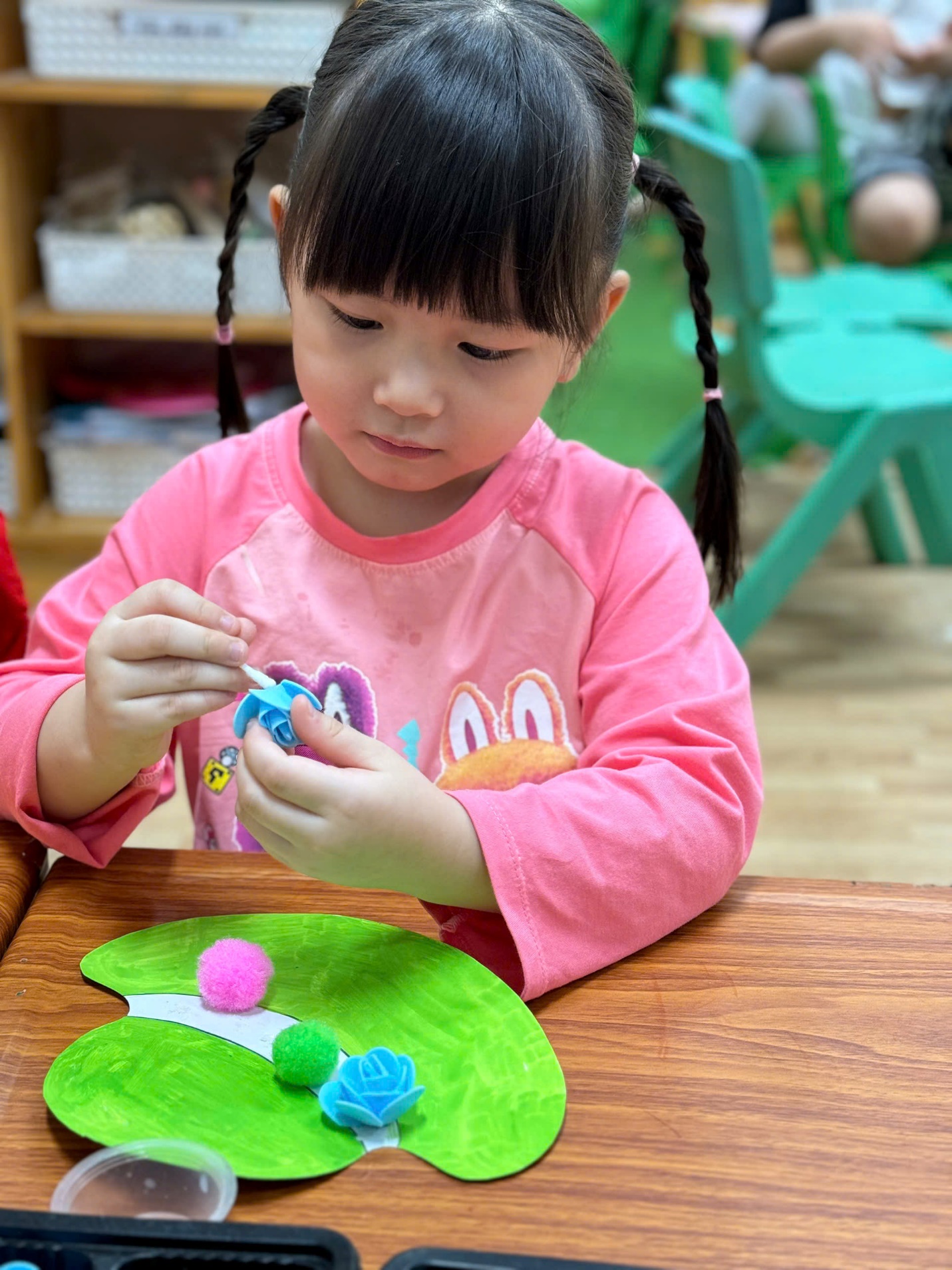 A child sitting at a table with a green paper and a green plant

Description automatically generated