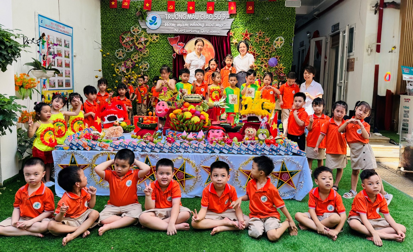 A group of children sitting on the ground in front of a table with a stage and a person in the background

AI-generated content may be incorrect.